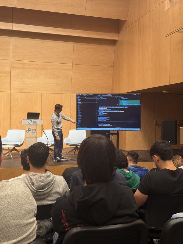 Ponente durante una charla de desarrollo asistido por IA, con código proyectado en pantalla